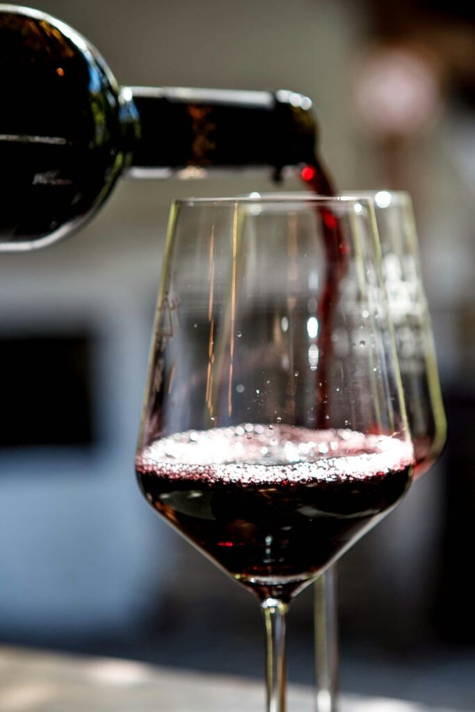 Close-up of red wine being poured into a glass, showcasing rich color and bubbles.